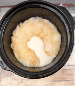 soap batter in a slow cooker with light liquid sitting on top in the center separated from the rest of the mix